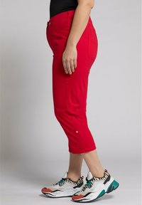 Pantalons rouges courts en tissu léger avec des poches latérales et une taille ajustée, associés à des baskets volumineuses multicolores.