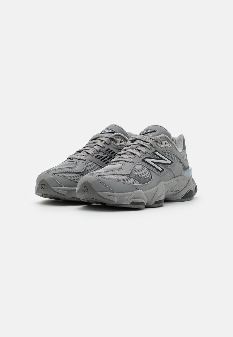 Graue Sportschuhe mit einem Obermaterial aus Mesh, gepolstertem Kragen und Gummisohle. Merkmale ein dezentes geometrisches Muster und eine signatur Branding an der Seite.