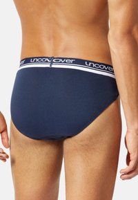 Marineblaue Baumwollslips mit einem weißen Bund, auf dem der Markenname "uncover" steht. Das Design ist eng anliegend und nahtlos am Rücken.