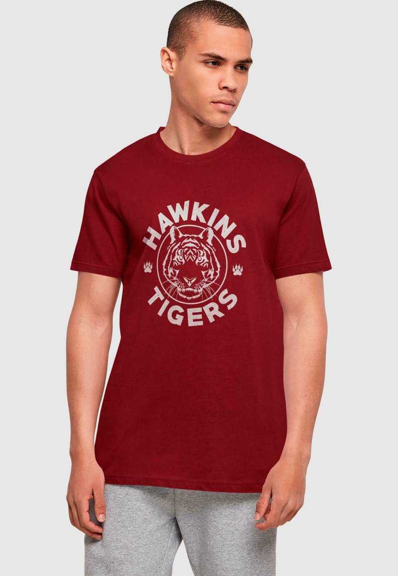 Vyno raudonas medvilnės marškinėliai su grafika, vaizduojančia tigro veidą, ir tekstu "HAWKINS TIGERS" pilka spalva, trumpomis rankovėmis ir apvalia iškirpte.