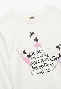 Hvid sweatshirt med legende grafikker af dansere i lyserøde nederdele og et motiverende citat, med en blød tekstur og rund halsudskæring.