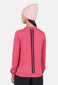 Różowy sweter dzianinowy z prążkowanym kołnierzem i mankietami, pionowymi czarnymi paskami na plecach oraz dopasowanym krojem. W połączeniu z teksturowaną różową czapką.