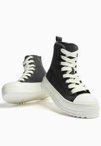 Czarne trampki za kostkę z płóciennego materiału, z białymi sznurowadłami, masywną białą podeszwą i teksturowanym wzorem bieżnika. Zaokrąglony nosek i przeszycia jako detale.