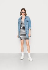 Jaqueta de ganga, vestido xadrez e botas brancas até ao tornozelo. O conjunto apresenta um padrão em preto e branco e um corte descontraído.