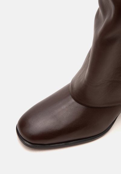 Bottine en cuir marron foncé avec un bout arrondi et une semelle noire sur fond blanc.