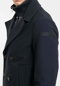 Marineblauw dubbel-breasted jas met een gestructureerde kraag, textuur met hoge nekvoering en zwarte knopen. Voorzien van een klein logopatch op de mouw.