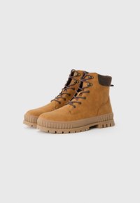 Botas de tobillo de ante marrón con cuello de tela marrón texturizada, puntera redonda y suela de goma rugosa de color marrón claro con surcos profundos y diseño de cordones.