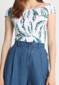 Bílý top s potiskem zelených palmových listů, elastický výstřih bez ramínek; spárovaný s modrými džínovými šortkami s vysokým pasem a sklady.