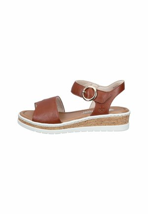 Brown leather sandal with wide toe strap, ankle strap featuring a round gold buckle, cork wedge sole, and white rubber outsole.