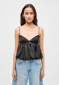 Czarny satynowy top z głębokim dekoltem, cienkimi ramiączkami i marszczonym stanem w stylu peplum. W zestawieniu z jasnoniebieskimi dżinsami.