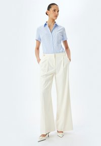 Lichtblauw gestreept overhemd met knopen, gecombineerd met witte wijdlopende broek, met een dubbele knoopdetail bij de taille en elegante witte hakken.