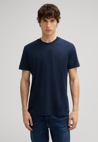 Marineblauwe crewneck t-shirt van zachte katoen, met korte mouwen en een rechte pasvorm, gecombineerd met donkerblauwe jeans.