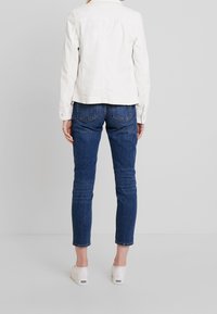 White denim jacket with a collared neckline, paired with dark blue slim-fit jeans, and white canvas slip-on shoes.