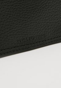 Portafoglio in pelle nera con superficie testurizzata, caratterizzato da un logo in rilievo sottile. Bordi puliti e cuciture accurate.