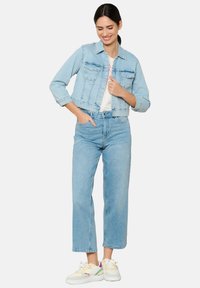 Hele sinine teksajakk, millel on lühendatud disain, kaks rinna/taskut, koos kõrge vöökohaga hele siniste teksade ja värviliste tossudega.