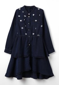 Tummansininen pitkähihaisessa kerrosmekossa on valkoista kukka-ompelua, etupainonappisuljenta, kaksi rintataskua ja kerrottu vyötärö.