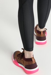 Czarne legginsy teksturowane z siateczkowymi detalami oraz brązowe buty sportowe z różowymi akcentami i białą podeszwą.