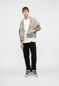 Hallhallik, millel on ees taskud, valge T-särk all, mustad püksid ja sinised kõrge säärega tenni, millel on tekstuuriga paelad.