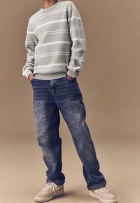 Sweatshirt à rayures grises avec un col rond, associé �à un jean bleu ample. Les chaussures arborent une palette de couleurs grise clair et beige.