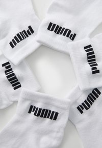 Vita bomullssockor arrangerade i en cirkel, med svart "PUMA"-logotyp broderad på mudden. Mjuk textur, ribbad design.