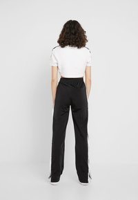 Korta vita t-shirts och svarta träningsbyxor med vita sidosträck. Tyget ser slätt ut; byxorna har resårlinning.