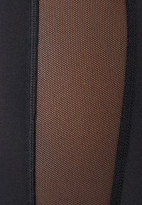 Tissu sportif noir comprenant un panneau en maille texturée, présentant un motif en nid d'abeille, et contrastant avec des bords et des coutures unis.