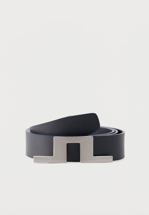 Cintura nera in pelle arrotolata con fibbia geometrica opaca in argento su uno sfondo chiaro e uniforme.