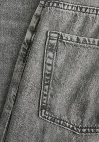 Pilkas džinsinis audinys su užpakaline kišene, pasižymintis išblukusiu tekstūromis, matomomis siūlėmis ir švariu apdaila.