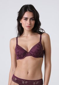 Bra in pizzo bordeaux con coppe sagomate e spalline regolabili, caratterizzato da motivi floreali e un piccolo dettaglio hardware centrale.