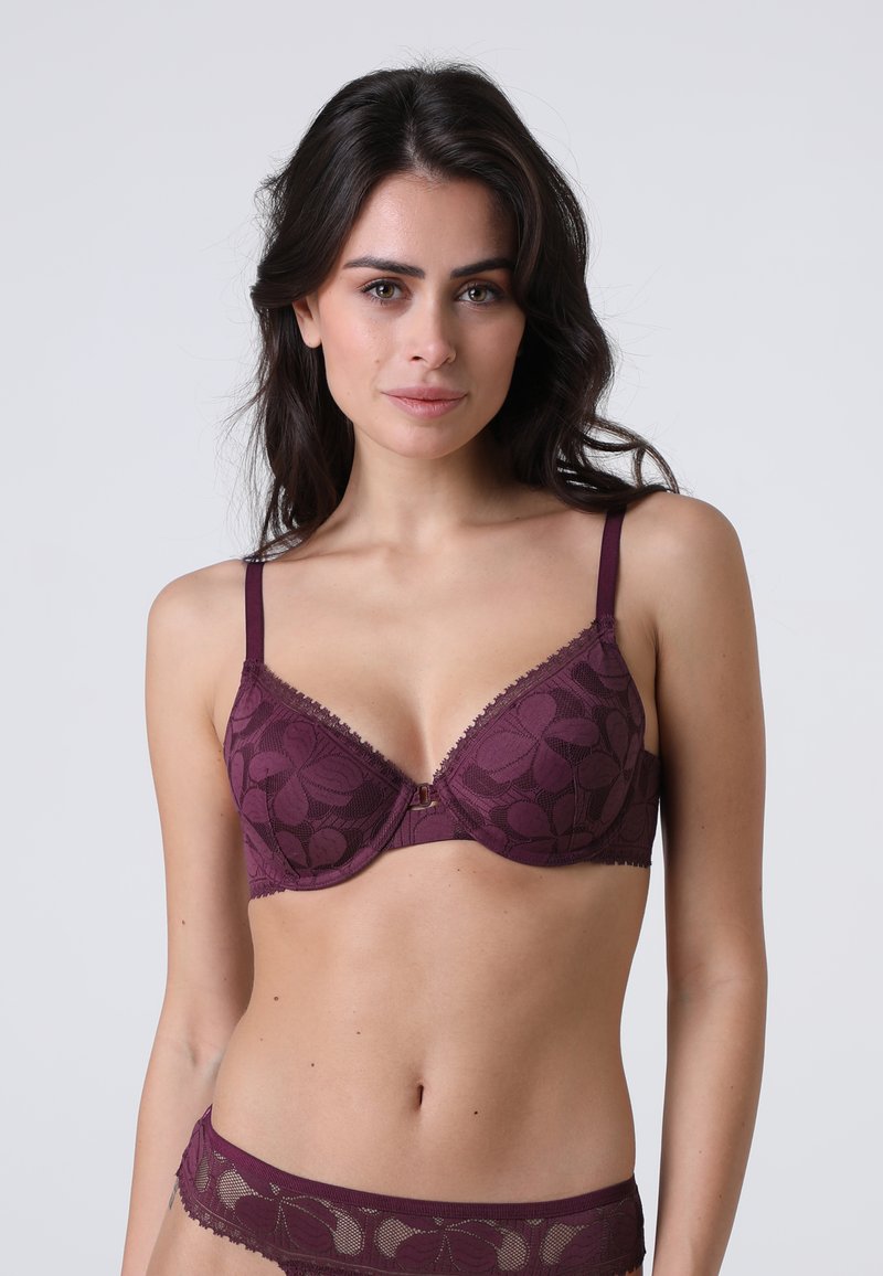 Bra in pizzo bordeaux con coppe sagomate e spalline regolabili, caratterizzato da motivi floreali e un piccolo dettaglio hardware centrale.