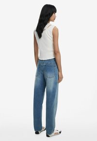 Witte geribde tanktop gecombineerd met lichtblauwe wijde denim jeans. De jeans hebben een gradient effect en twee achterzakken. Casual platte schoenen.