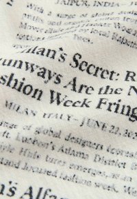 Gros plan sur un tissu froissé imprimé de texte noir ressemblant à un article de journal ou de magazine.