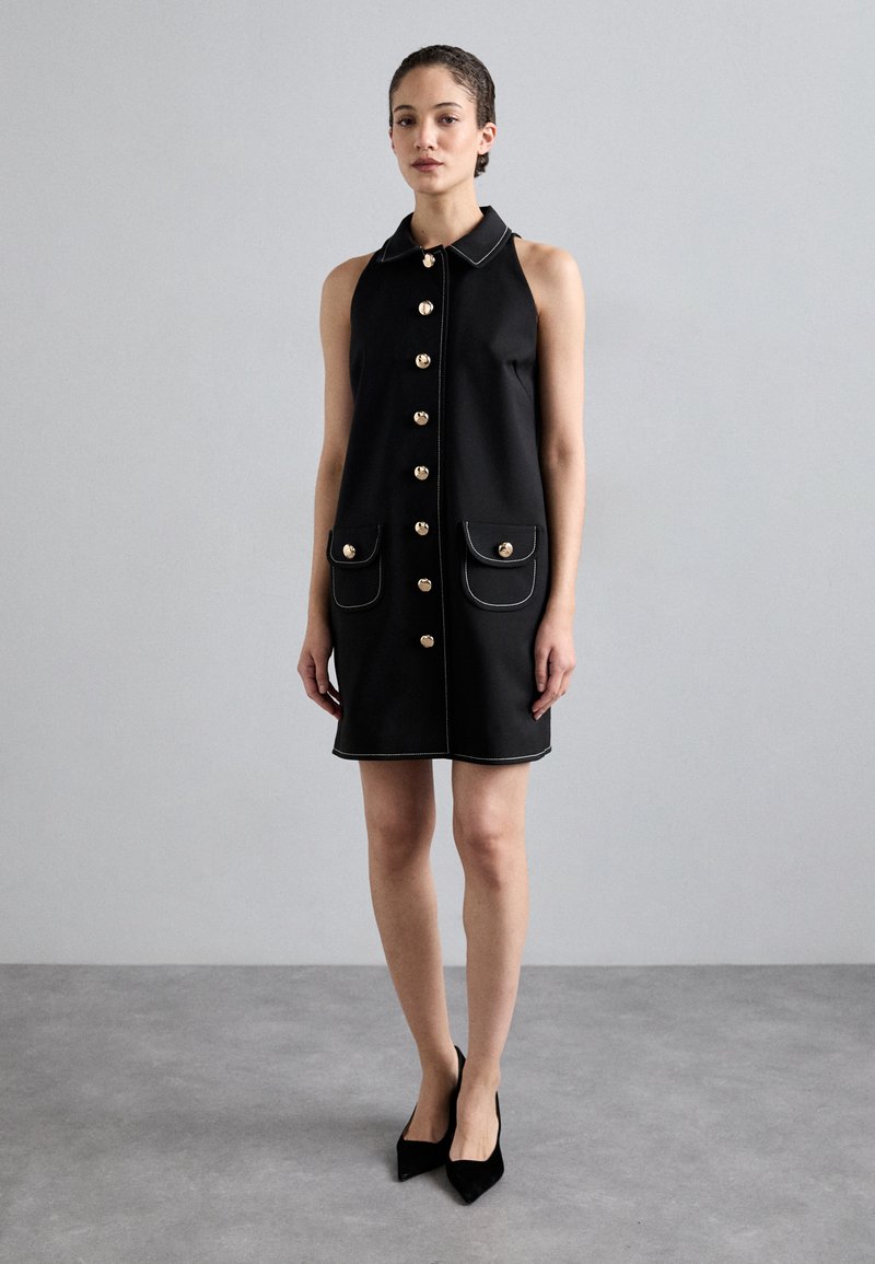 Black sleeveless dress with a collar, gold button front, two front pockets, and white stitching accents. Soft material with a smooth texture.
