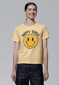 Geel katoenen T-shirt met een ronde smiley face grafiek en de tekst "HAPPY TIMES" in het zwart, korte mouwen en een relaxte pasvorm.
