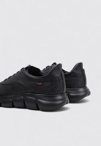 Zapatillas de cuero negro con suela de goma redondeada, textura suave, costuras mínimas y un sutil logo en el lateral.