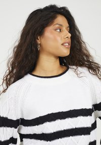 Sweter dziewiarski w biało-czarne paski z prążkowanym dekoltem, zdobiony teksturowanymi wzorami w diamenty na czarnych paskach.