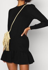 Black long-sleeve dress with a flared hem, featuring gathered puffed shoulders. Accompanied by a small beige leather fringed bag.