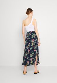 Floral maxi skirt with a navy background, featuring a side slit, paired with a white one-shoulder top and casual sandals.