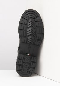 Zwarte rubberen schoenzool met een gestructureerd, multidirectioneel loopvlakpatroon voor grip, met gegraveerd merk en een detail van de Italiaanse vlag.