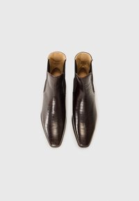 Bottines en cuir marron avec une texture crocodile, à bout pointu et côtés ouverts, dotées d'une doublure intérieure lisse et d'un design minimaliste.