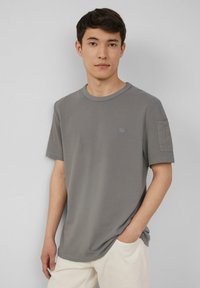 Grijze korte mouwen t-shirt van een zachte, gestructureerde stof met een ronde hals en een klein accentdetail op de linkermouw.