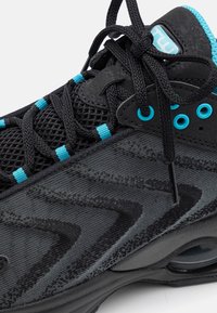 Svart sportskor med mesh- och släta tyger, turkosa accenter, intrikata mönster och en rundad sula med synlig luftdämpning.