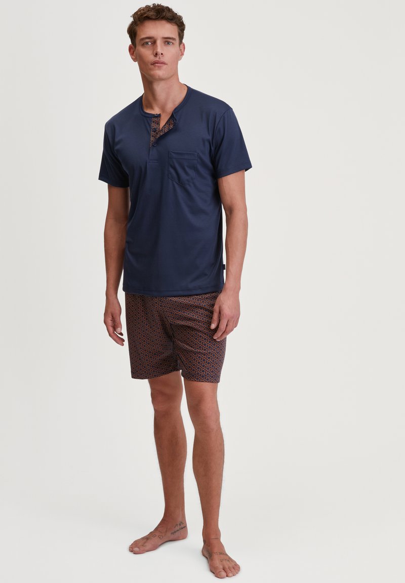 Marineblauwe kortemouwen overhemd met een knoopsluiting bij de hals en een borstzak, gecombineerd met gemusterde shorts in oranje en marineblauw. Glad materiaal, casual ontwerp.