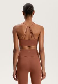 Bra top and leggings in rust color. Features thin straps and a fitted design. Material is smooth with a subtle sheen. Logo at the waistband.