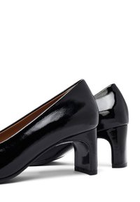 Scarpe con tacco alto in pelle verniciata nera, con punta arrotondata e tacco a blocco. La superficie è lucida e presenta una texture liscia, evidenziando un design minimalista.