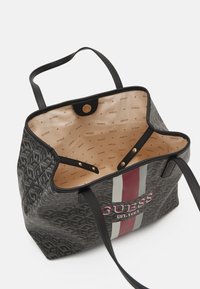 Mustat kantokassi, jossa on kuvioitu ulkopinta, kontrastivärit punaiset ja harmaat raidat, sekä vaaleanruskea sisustus, jossa on logoprintti. Magneettisulku ja tukevat kahvat.