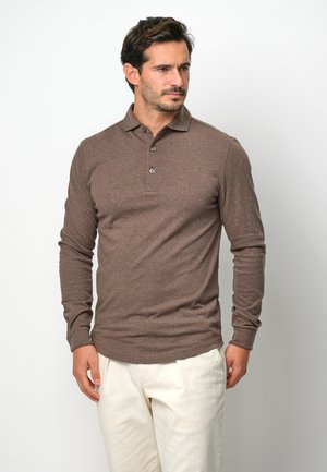 Brown long-sleeve polo shirt with a collar and three button placket, made of soft fabric. Worn with light-colored trousers.