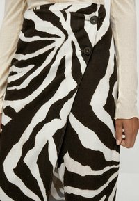 Gonna a stampa zebra realizzata in tessuto leggero, con un design avvolgente, strisce nere e bianche e due bottoni neri in vita.