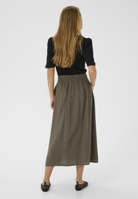 Jupe longue couleur olive fabriquée en tissu léger avec une taille élastique, associée à un haut noir ajusté. Conception simple et fluide.
