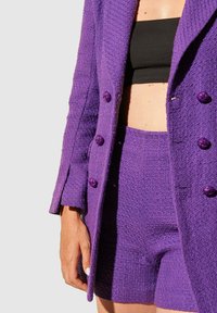 Blazer texturé violet avec short assorti. Le blazer présente deux grands boutons noués et un col cranté. Le tissu semble épais et tissé.